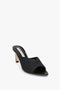 Victoria Beckham's V Cut Mule In Black Raffia features a mid-height heel and an open-toe design. The heel has a metallic accent and the textured raffia adds an elegant touch.