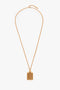 A gold necklace with a rectangular, gold brushed brass pendant featuring vertical grooves, reminiscent of the Victoria Beckham Exclusive Perfume Bottle Necklace In Brushed Gold.