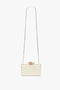 A small rectangular white Frame Flower Minaudiere Bag in Chamomile with a gold chain strap and a decorative gold flower on top, perfect for accessorizing like Victoria Beckham.