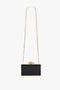 A rectangular black clutch with a gold chain strap and an ornate flower clasp on top was replaced with the Victoria Beckham Frame Flower Minaudiere Bag in Black.