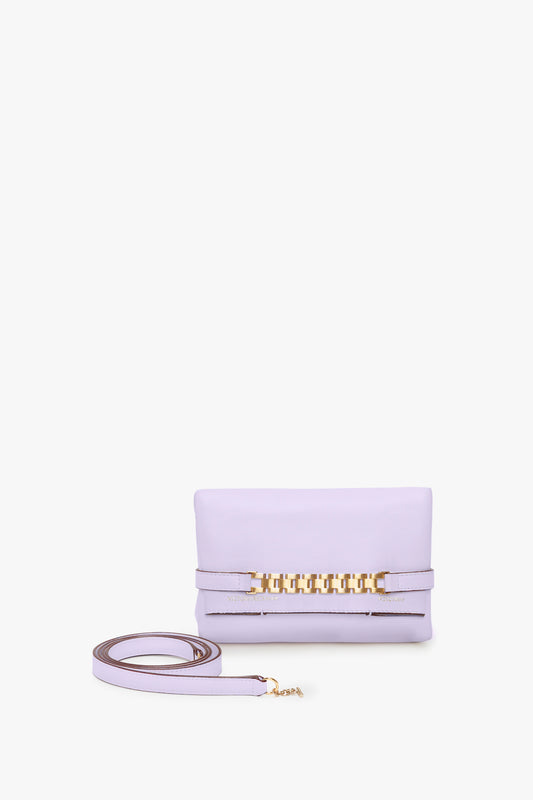 A light lilac leather Victoria Beckham EXCLUSIVE Mini Chain Pouch With Long Strap In Lilac Leather with a gold-tone chain detail on the front and a matching detachable strap placed beside it.
