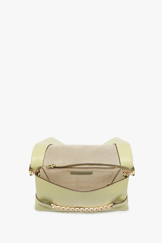 The Victoria Beckham Chain Pouch With Strap In Avocado Leather features a light green exterior with a top zipper and a beige suede panel. At the bottom, it boasts a gold chain and leather strap detail, giving this Chain Pouch With Strap In Avocado Leather an elegant touch.