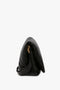 Side view of a black, slouchy Puffy Jumbo Chain Pouch In Black Leather by Victoria Beckham with a gold clasp and an adjustable shoulder strap against a white background.