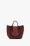 A Victoria Beckham W11 Medium Tote Bag In Burgundy Leather with two short handles, a structured design, and a small embossed logo near the bottom edge, perfect for versatile styling.