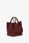 A large, dark red grained leather W11 Medium Tote Bag In Burgundy Leather with a structured design and dual top handles, angled on a white background. The versatile styling makes it perfect for any occasion by Victoria Beckham.