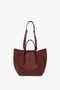 A W11 Medium Tote Bag In Burgundy Leather by Victoria Beckham, crafted from grained leather, featuring two wide shoulder straps and a large central compartment, perfect for versatile styling.