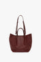 A W11 Medium Tote Bag In Burgundy Leather by Victoria Beckham featuring two handles and a detachable shoulder strap, perfect for versatile styling, against a white background.