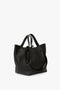 A W11 Medium Tote Bag In Black Leather with two shoulder straps, featuring a minimalist design and subtle gold-tone accents, reminiscent of Victoria Beckham's elegant style.