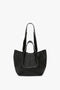 A black grained leather tote bag with two shoulder straps, featuring a minimalist design. Perfect as a W11 Medium Tote Bag In Black Leather for everyday use, this stylish accessory aligns with the sophisticated aesthetics of Victoria Beckham.