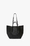 A W11 Jumbo Tote Bag In Black Leather crafted from luxury grained leather by Victoria Beckham, featuring dual top handles, a structured design, and small gold-colored brand inscriptions near the bottom.