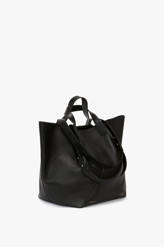 A luxury black leather Victoria Beckham W11 Jumbo Tote In Black Leather with dual adjustable straps and minimal gold-toned hardware details is set against a plain white background. It features an internal pocket compartment, perfect for organized storage.