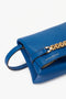 A close-up image of a Sapphire blue leather handbag with a gold chain detail and a small handle. The brand name Victoria Beckham UK is embossed on the bag. This Mini Chain Pouch Bag With Long Strap In Sapphire Blue also features a convenient detachable strap.