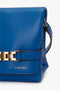 Close-up of a Mini Chain Pouch Bag With Long Strap In Sapphire Blue by Victoria Beckham UK with a gold chain detail and the label "N°202VB011" embossed on the bottom section. The mini chain pouch also features a detachable strap for added versatility.