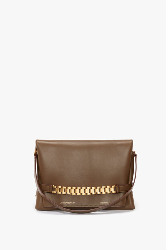 A brown rectangular Nappa leather handbag with a gold chain decoration and a single detachable brown strap. The words "Victoria Beckham UK" are embossed near the bottom in gold, embodying the elegance of a Chain Pouch Bag With Strap In Khaki Leather.