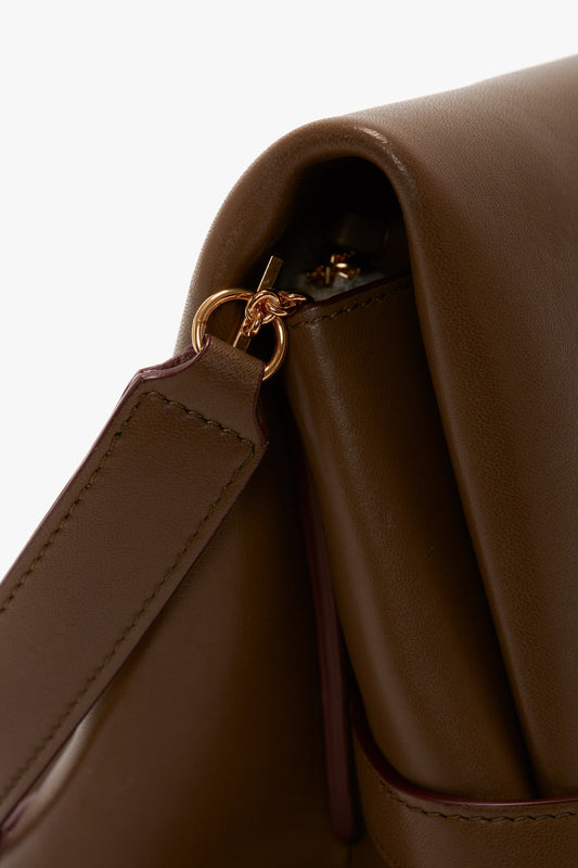 Close-up of a brown Victoria Beckham UK Chain Pouch Bag With Strap In Khaki Leather showcasing a gold ring attachment where the detachable strap connects to the bag.