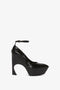 A black high-heeled shoe with a pointed toe, textured surface, and an ankle strap. The heel is wide and arched, crafted in embossed croc leather for added elegance— the Ankle Strap Wedge Pump In Black Croc-Effect Leather by Victoria Beckham.