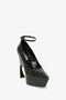 A single dark green, embossed croc leather pump with a chunky platform, sculptural heel, and an ankle strap. The shoe is angled slightly to the left. Introducing the Ankle Strap Wedge Pump In Dark Green Croc-Effect Leather by Victoria Beckham.