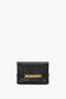 A black Mini Chain Pouch Bag With Long Strap In Black Leather with a gold chain detail on the front and the text "Victoria Beckham" printed in gold at the bottom left.