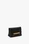 A black lambskin leather clutch with a gold chain detail and the words "VICTORIA BECKHAM" engraved on the front. The sleek, minimalist Mini Chain Pouch Bag With Long Strap In Black Leather by Victoria Beckham is perfect for any occasion.