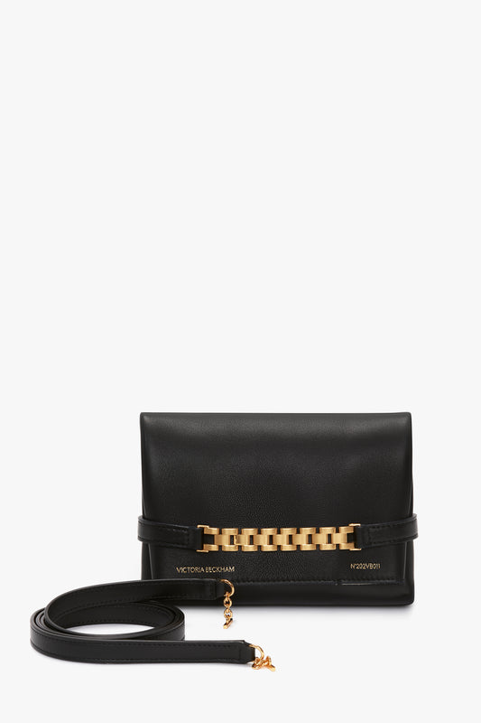 A black lambskin leather designer clutch bag with a detachable strap and gold chain detailing on the front. The brand name is visible on the bottom center of the bag, reflecting its premium craftsmanship akin to a Mini Chain Pouch With Long Strap In Black Leather by Victoria Beckham.