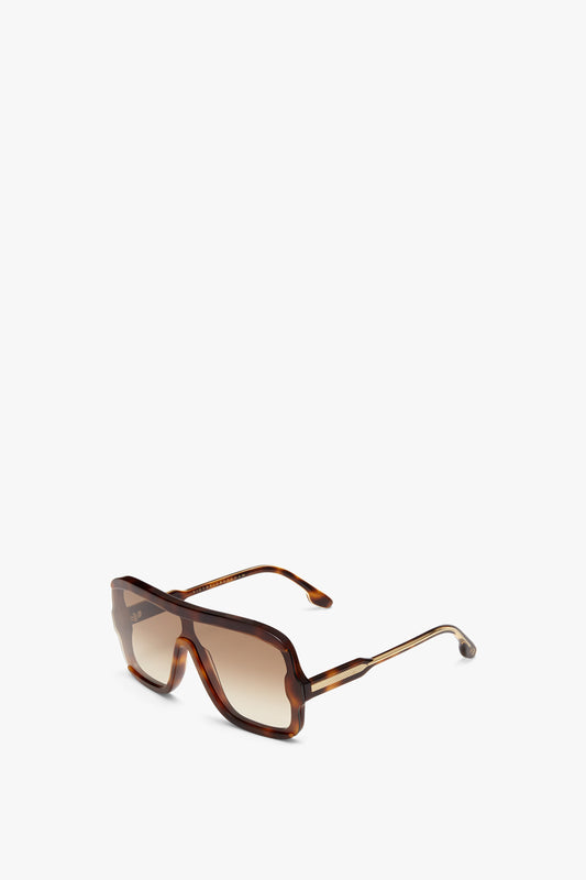 A pair of brown oversized rectangular sunglasses with graduated brown lenses, featuring a thick frame and slender arms, displayed on a white background. Layered Mask Sunglasses In Tortoise-Brown by Victoria Beckham.