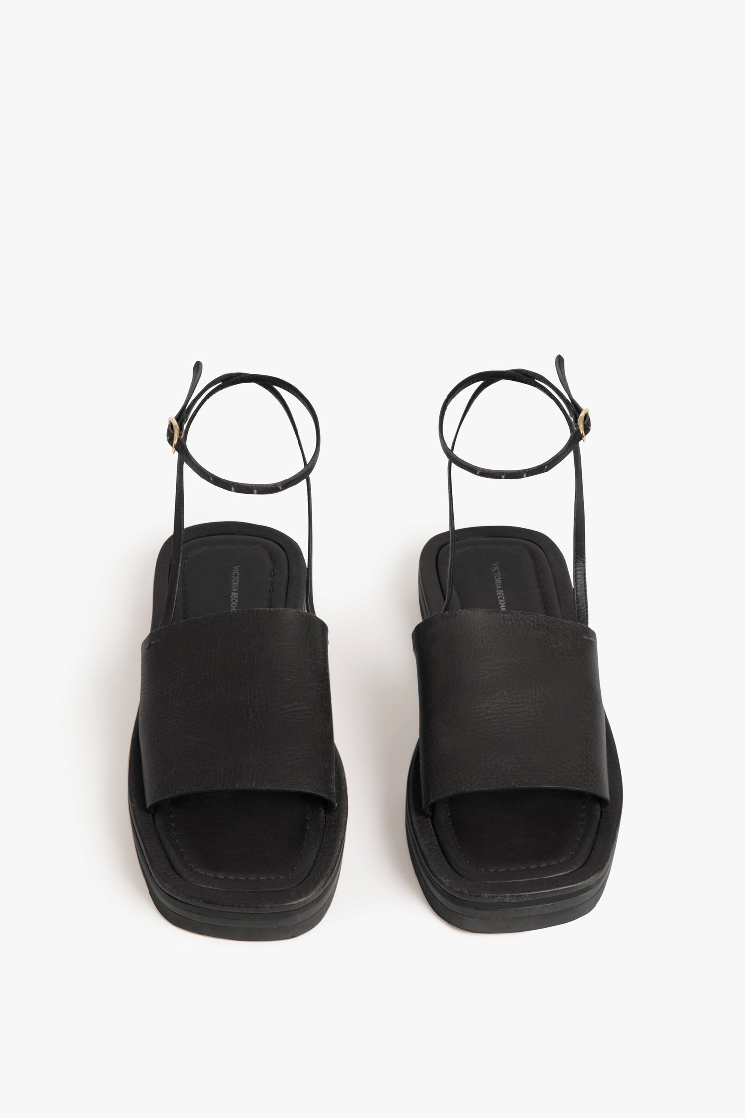 A pair of black Frances Sandal in Black by Victoria Beckham with wide straps, ankle straps, and a peep-toe design, featuring a minimalist leather band, displayed against a white background.