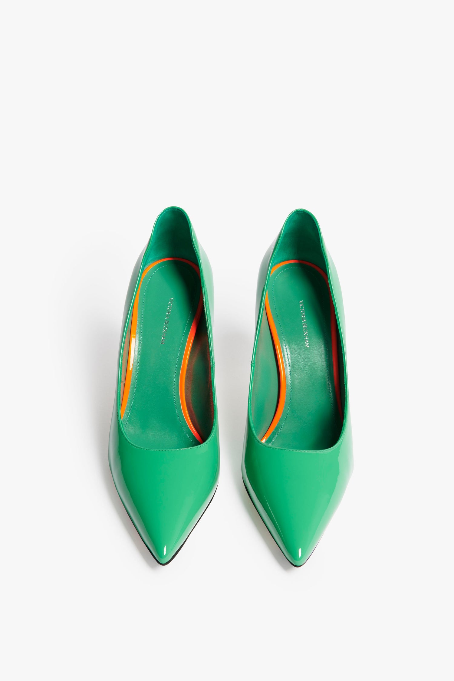 A pair of jade green patent leather high-heeled shoes with pointed toes. The insoles are orange and green, featuring the Victoria Beckham brand name visibly on the insole. These chic VB 90mm Pump In Jade boast a sophisticated 90mm stiletto heel.