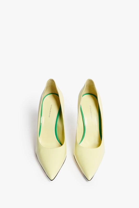 A pair of light yellow, pointed-toe high-heeled shoes with green insoles and a 90mm stiletto heel, placed on a white background. These VB 90mm Pump In Pale Lemon by Victoria Beckham are a wardrobe essential for any fashion-forward individual.