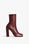 The Iona Boots In Dark Red by Victoria Beckham feature an ankle-high silhouette with a high block heel and a slightly squared toe profile, set against a plain white background.