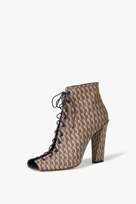 The Victoria Beckham Reese Boots In House Monogram Jacquard are high-heeled, lace-up booties with a chic peep toe design, showcasing a stylish tan and black pattern with a repeating monogram print.