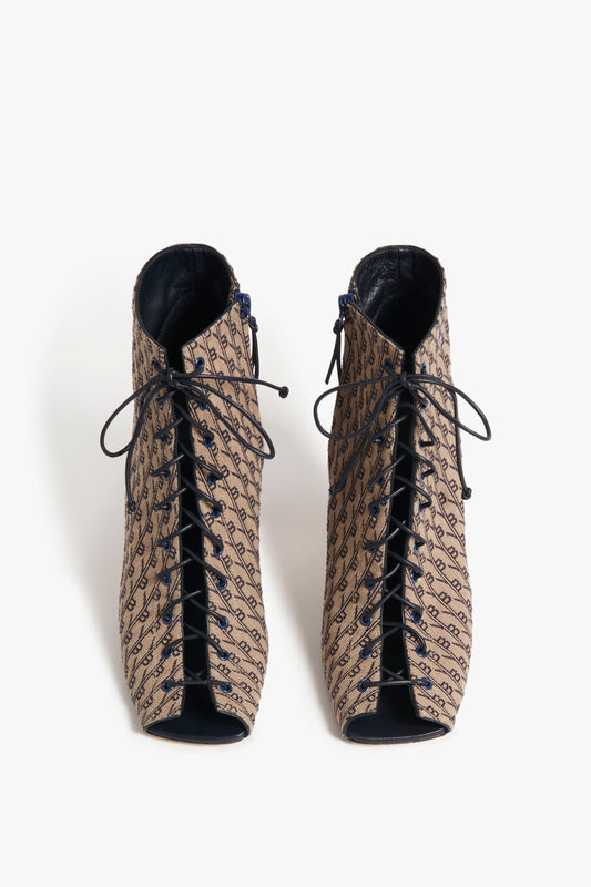 A pair of Reese Boots In House Monogram Jacquard by Victoria Beckham in beige, featuring a monogram print and peep toe design, viewed from the front.