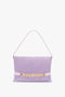 A Victoria Beckham Chain Pouch Bag with Strap in Lilac Suede featuring a short handle and gold chain detail across the front.