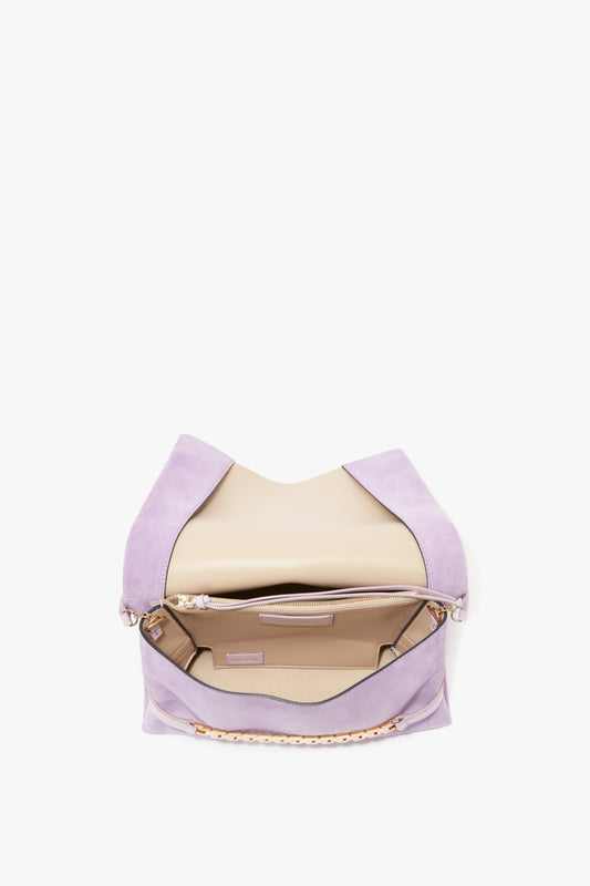 Image of an open pastel purple bag with a beige interior, showcasing two compartments and a zippered suede pouch inside. The bag shown is the Chain Pouch with Strap in Lilac Suede by Victoria Beckham.