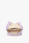 A top-view image of an open Victoria Beckham Chain Pouch Bag with Strap in Lilac Suede, revealing a beige interior with a zippered pocket, crafted from luxurious Italian leather.