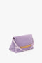 A Chain Pouch Bag with Strap in Lilac Suede by Victoria Beckham, designed in a fold-over pouch bag style, featuring a gold chain detail on the front and a single shoulder strap.