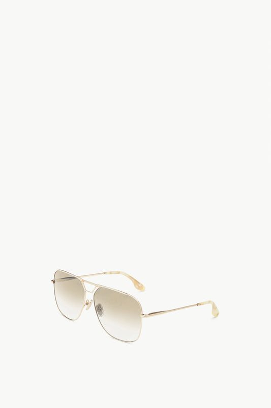 A pair of Victoria Beckham Classic V Metal Navigator Sunglasses in Gold with thin, gold-coloured metal frames and gradient lenses, featuring tortoise acetate tips, positioned on a white background.