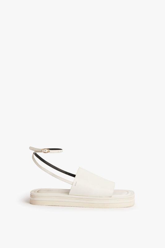 A single Frances Sandal in White by Victoria Beckham, with a flat sole, an ankle strap, and a thick strap over the foot, reminiscent of a 90s aesthetic, displayed against a plain white background.