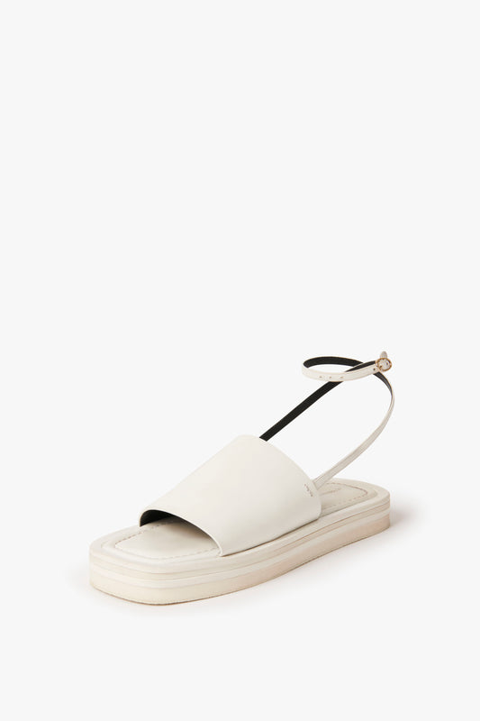 The Victoria Beckham Frances Sandal in White embodies a 90s aesthetic with its chunky, thick flat sole and open toe design. A black ankle strap featuring a small buckle completes this stylish white sandal.
