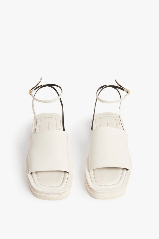 A pair of white open-toe Frances Sandal in White from Victoria Beckham with wide straps and thin ankle straps viewed from above against a white background, exuding a subtle 90s aesthetic.