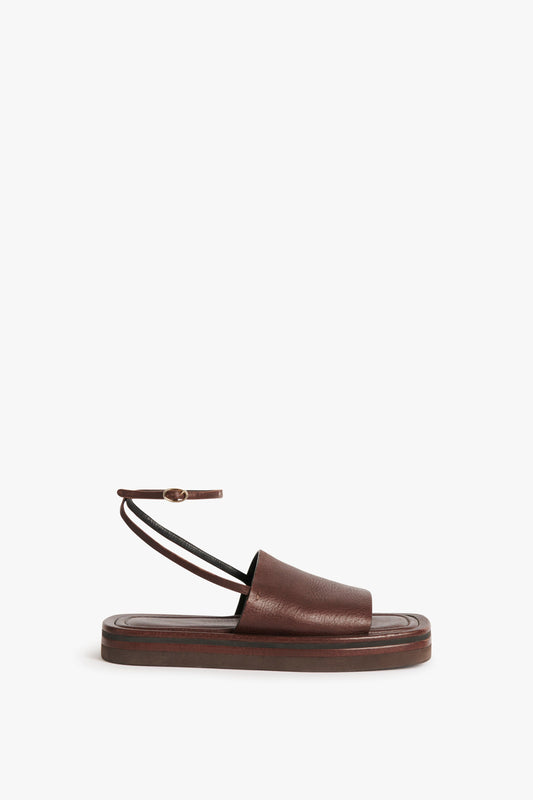 The Frances Sandal in Dark Brown by Victoria Beckham is a single brown leather and EVA masterpiece with a flat sole, featuring an ankle strap with a small buckle, channeling that timeless 90s aesthetic.