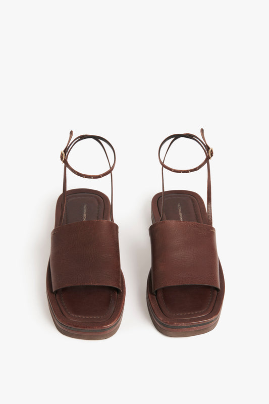 The Frances Sandal in Dark Brown by Victoria Beckham, embodying a 90s aesthetic, features brown leather and EVA with thick straps and ankle buckles, displayed on a plain white background.