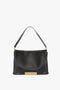 Black Nappa leather handbag with a gold geometric clasp and a single shoulder strap against a plain white background. This Jumbo Chain Pouch Bag In Black Leather by Victoria Beckham also features a detachable strap for added versatility.