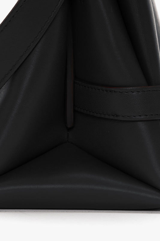 Close-up image of a black Nappa leather accessory, showing a triangular shape with fine stitching and a strap detail, ideal for versatile styling. Chain Pouch with Strap In Black Leather by Victoria Beckham.
