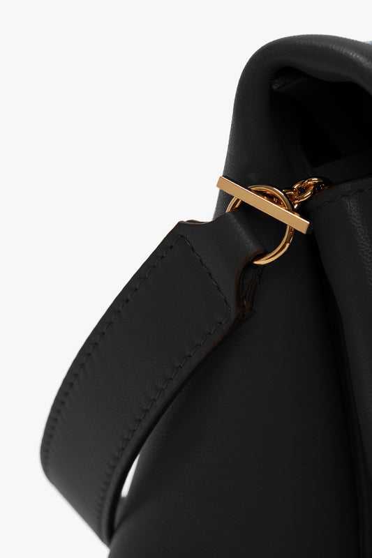 Close-up of a Victoria Beckham Chain Pouch with Strap In Black Leather's strap attachment featuring a gold ring clasp against a plain white background, showcasing its versatile styling.