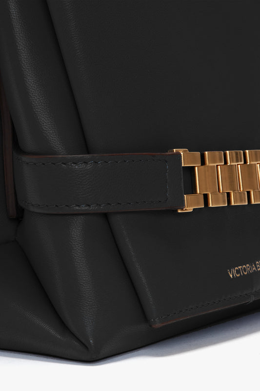 Close-up of a black Nappa leather Chain Pouch with Strap In Black Leather featuring a gold chain link detail and a subtle "Victoria Beckham" inscription on the lower right corner, perfect for versatile styling.