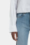 A person in a white Cropped Patch Pocket Shirt In White by Victoria Beckham and blue jeans stands with their left arm hanging by their side.