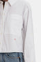 Close-up of a person wearing a white Cropped Patch Pocket Shirt In White by Victoria Beckham with a red embroidered initial "AB" above the blue jeans waistband, reminiscent of Victoria Beckham's style.