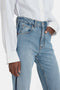 A person wearing a white Victoria Beckham Cropped Patch Pocket Shirt In White and high-waisted blue jeans, with one hand in their pocket.