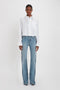 A person wearing a Cropped Patch Pocket Shirt In White by Victoria Beckham and blue jeans stands against a plain white background.