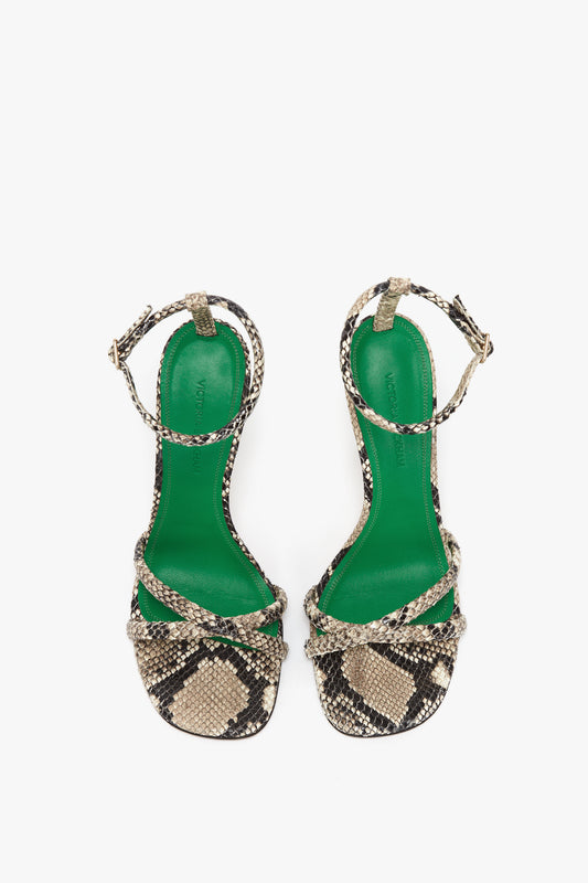 A pair of Victoria Beckham Anne Sandal In Cream Printed Snakeskin high-heeled sandals with a green insole and snake-print straps, featuring smooth leather ankle straps and crisscross toe straps, against a white background, exuding high-octane appeal.